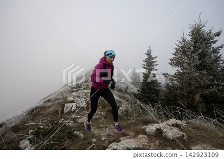 Female Trail Runner In Frosty Fog Running Along Rocky Mountain Ridge With Headlamp And Backpack Female Trail Runner In Frosty Fog Running Along Rocky Mountain Ridge With Headlamp And Backpack 142923109