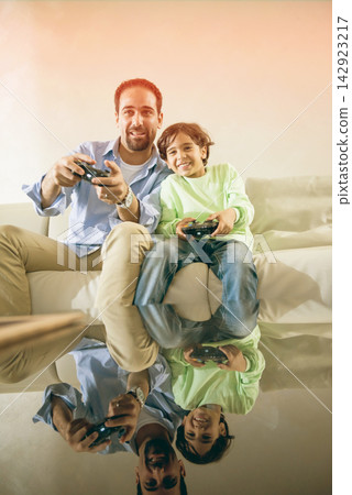 Middle Eastern father and son playing video games together at home, modern Arab family bonding Middle Eastern father and son playing video games together at home, modern Arab family bonding 142923217