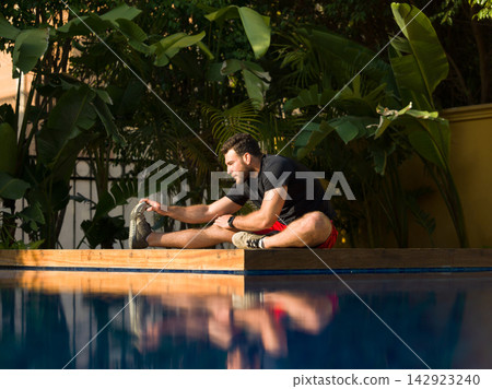Man stretching by poolside at a modern luxury villa for morning fitness and recovery Man stretching by poolside at a modern luxury villa for morning fitness and recovery 142923240