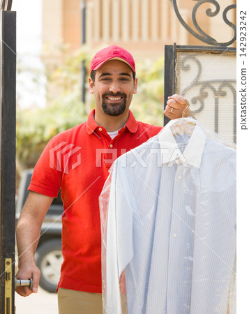 Smiling delivery man drops off dry-cleaned shirt at gate of modern multigenerational family villa Smiling delivery man drops off dry-cleaned shirt at gate of modern multigenerational family villa 142923242