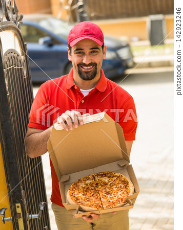 Smiling delivery man handing pizza boxes to Middle Eastern multi generation family at modern luxury villa 142923246