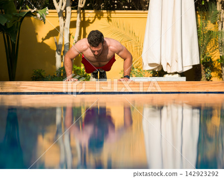 Man doing push-ups by a luxury villa pool during a family stay at a modern multigenerational home Man doing push-ups by a luxury villa pool during a family stay at a modern multigenerational home 142923292
