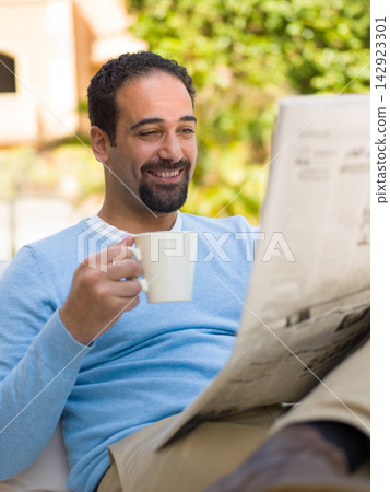Middle Eastern man relaxing with coffee and newspaper on a luxury villa patio as part of multigenerational family Middle Eastern man relaxing with coffee and newspaper on a luxury villa patio as part of multigenerational family 142923301