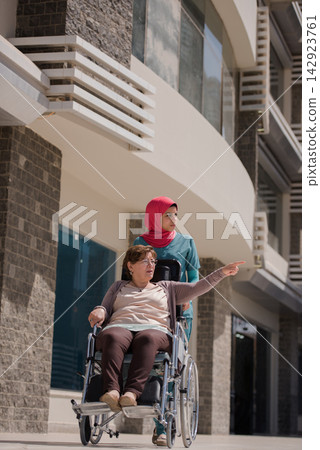 Nurse in hijab assisting elderly patient in wheelchair outside a modern Middle Eastern eye hospital in Egypt 142923761