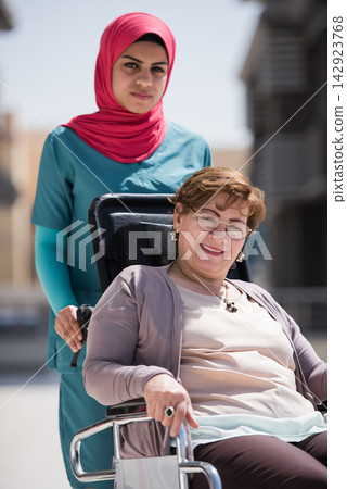 Middle Eastern nurse pushing smiling senior patient in wheelchair outside eye hospital clinic in Egypt 142923768