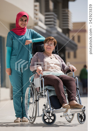 Middle Eastern nurse with patient in wheelchair outside eye hospital clinic in Egypt providing compassionate healthcare support Middle Eastern nurse with patient in wheelchair outside eye hospital clinic in Egypt providing compassionate healthcare support 142923839