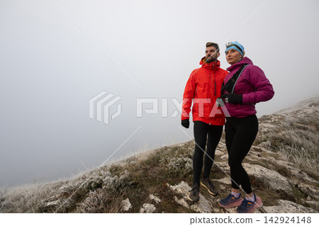 Hiking Couple Standing on Foggy Mountain Ridge in Winter Jackets With Headlamps and Trail Shoes Hiking Couple Standing on Foggy Mountain Ridge in Winter Jackets With Headlamps and Trail Shoes 142924148