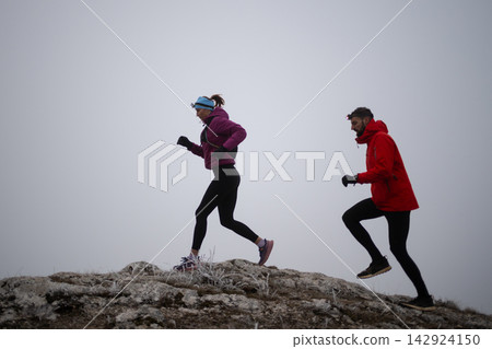 Trail Running Couple Jogging on Foggy Winter Mountain Ridge Wearing Headlamps and Outdoor Gear Trail Running Couple Jogging on Foggy Winter Mountain Ridge Wearing Headlamps and Outdoor Gear 142924150