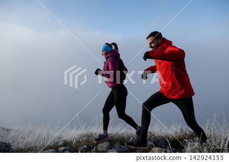 Couple Trail Running in Winter Mountains Wearing Warm Jackets and Outdoor Fitness Gear Couple Trail Running in Winter Mountains Wearing Warm Jackets and Outdoor Fitness Gear 142924153