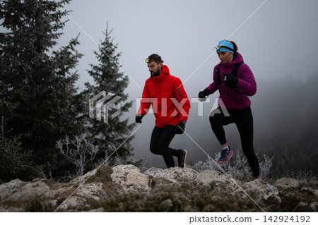 Trail Running Couple With Headlamps Through Foggy Winter Mountain Landscape at Dusk Trail Running Couple With Headlamps Through Foggy Winter Mountain Landscape at Dusk 142924192