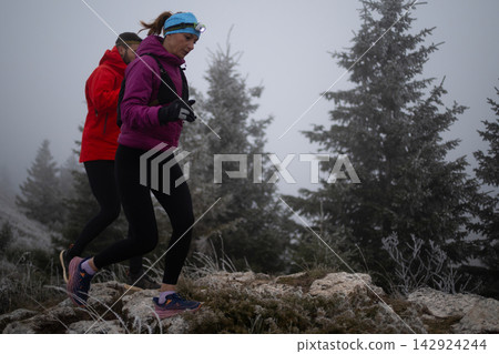 Two Women Trail Running in Frosty Fog With Headlamps on a Mountain Ridge at Dawn Two Women Trail Running in Frosty Fog With Headlamps on a Mountain Ridge at Dawn 142924244