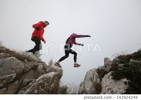 Couple Hiking and Jumping Across a Rocky Mountain Gap on a Foggy Winter Adventure 142924249