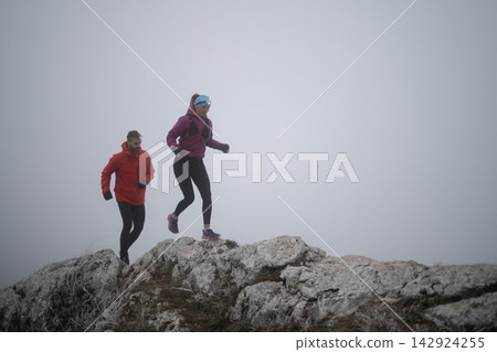 Couple Trail Running on Foggy Mountain Ridge Wearing Headlamps and Cold Weather Gear Couple Trail Running on Foggy Mountain Ridge Wearing Headlamps and Cold Weather Gear 142924255