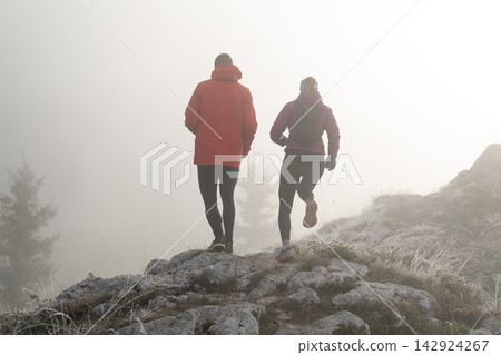 Couple Trail Running on Foggy Mountain Ridge in Winter Jackets for Outdoor Fitness Couple Trail Running on Foggy Mountain Ridge in Winter Jackets for Outdoor Fitness 142924267