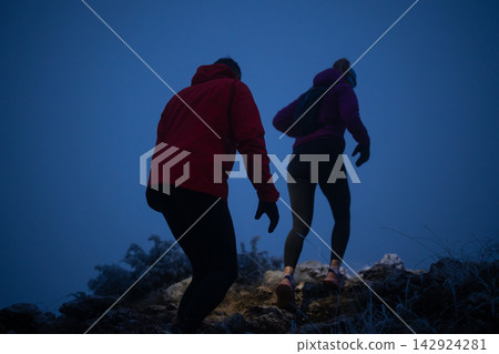Two Hikers Climbing a Rocky Trail at Dawn in Winter Jackets and Backpacks Two Hikers Climbing a Rocky Trail at Dawn in Winter Jackets and Backpacks 142924281