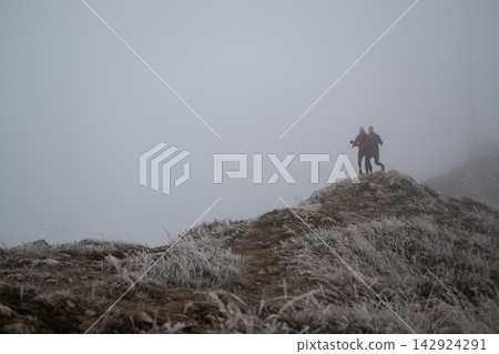 Couple Hiking On Frosty Mountain Ridge In Thick Fog With Headlamps At Dawn Couple Hiking On Frosty Mountain Ridge In Thick Fog With Headlamps At Dawn 142924291