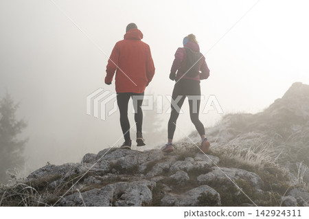 Couple Hiking on Rocky Ridge in Foggy Morning Trail Running Together in Cold Outdoor Adventure Couple Hiking on Rocky Ridge in Foggy Morning Trail Running Together in Cold Outdoor Adventure 142924311