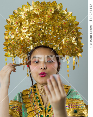 Young Indonesian Asian Woman In Traditional Thai Costume With Ornate Gold Headdress Applying Makeup Young Indonesian Asian Woman In Traditional Thai Costume With Ornate Gold Headdress Applying Makeup 142924352