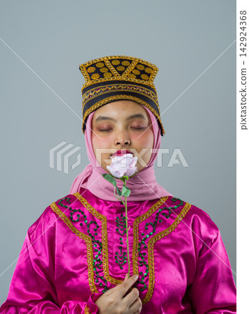 Young Indonesian Asian Woman In Pink Hijab And Traditional Headdress Holding A Rose With Eyes Closed Young Indonesian Asian Woman In Pink Hijab And Traditional Headdress Holding A Rose With Eyes Closed 142924368