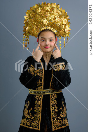Young Indonesian Asian Girl Wearing Ornate Gold Headdress And Embroidered Black Traditional Costume Portrait 142924371