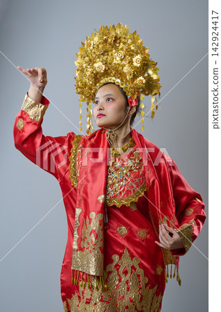 Indonesian Asian Woman Wearing Ornate Gold Headdress and Red Traditional Ceremonial Costume Posing Gracefully Indonesian Asian Woman Wearing Ornate Gold Headdress and Red Traditional Ceremonial Costume Posing Gracefully 142924417