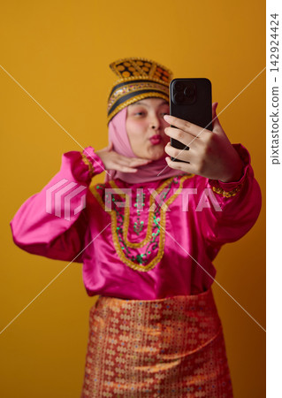Young Woman in Traditional Southeast Asian Costume and Hijab Taking a Colorful Selfie With Phone Young Woman in Traditional Southeast Asian Costume and Hijab Taking a Colorful Selfie With Phone 142924424