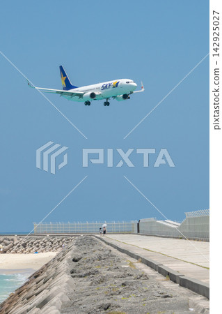 A Skymark aircraft making a low-altitude landing approach to Shimojishima Airport's 17END gate, against the backdrop of the emerald green sea. A Skymark aircraft making a low-altitude landing approach to Shimojishima Airport's 17END gate, against the backdrop of the emerald green sea. 142925027