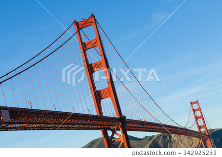 A view looking up at the main towers and cables of the Golden Gate Bridge against a blue sky background. A view looking up at the main towers and cables of the Golden Gate Bridge against a blue sky background. 142925231