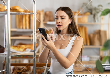 Young woman scanning pastry with her phone in bakery Young woman scanning pastry with her phone in bakery 142925384
