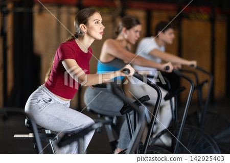 Focused girl works out with airbike during class at fitness club Focused girl works out with airbike during class at fitness club 142925403