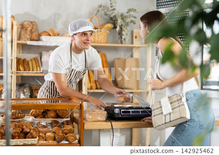 Guy puts croissants in transparent container, weighs goods and gives them to girl buyer Guy puts croissants in transparent container, weighs goods and gives them to girl buyer 142925462