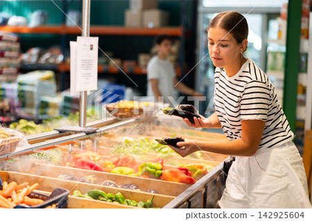 Interested young woman choosing organic ripe aubergines in farm store 142925604