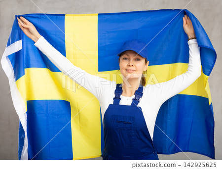 Smiling adult woman in uniform holding flag of Sweden Smiling adult woman in uniform holding flag of Sweden 142925625