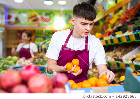 Man store employee displaying assortment of oranges at fruit department in supermarket Man store employee displaying assortment of oranges at fruit department in supermarket 142925665