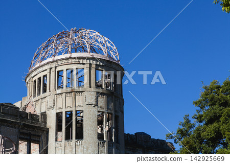 The exterior of the Atomic Bomb Dome stands out against the green trees and blue sky. The exterior of the Atomic Bomb Dome stands out against the green trees and blue sky. 142925669