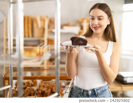 Positive young girl holding pastry on paper plate in bakery Positive young girl holding pastry on paper plate in bakery 142925802