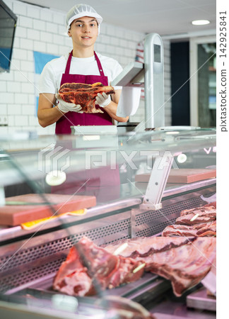 Positive young salesman demonstrating piece of meat in butcher shop Positive young salesman demonstrating piece of meat in butcher shop 142925841
