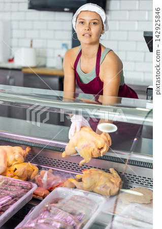 Positive young saleswoman demonstrating chicken in butcher shop Positive young saleswoman demonstrating chicken in butcher shop 142925846