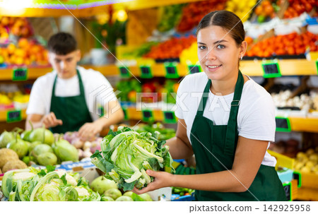 Hardworking young saleswoman puts cabbage on the counter Hardworking young saleswoman puts cabbage on the counter 142925958