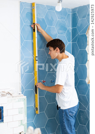 Man measuring flatness of wall with building level tool in new apartment during renovation Man measuring flatness of wall with building level tool in new apartment during renovation 142925973