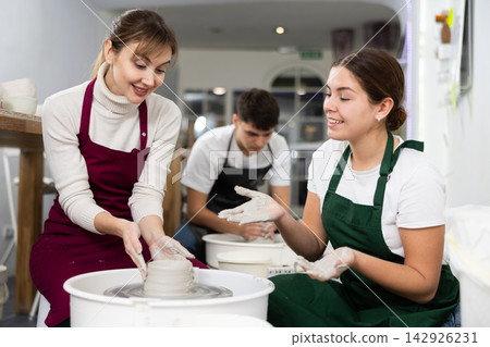 Two young women sculpt product on potter's wheel 142926231