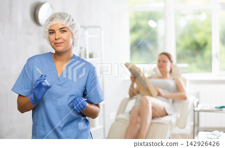 Nurse in disposable cap with syringe in hand and conducts preparatory activities before injections. Nurse in disposable cap with syringe in hand and conducts preparatory activities before injections. 142926426