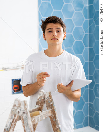 Man with documents in hands checks the quality of the completed repairs in cottage room Man with documents in hands checks the quality of the completed repairs in cottage room 142926479