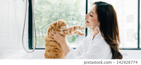 In the bathroom's tranquil atmosphere, a woman and her Scottish Fold cat share bath time, radiating happiness and the joy of maintaining hygiene and pet care. In the bathroom's tranquil atmosphere, a woman and her Scottish Fold cat share bath time, radiating happiness and the joy of maintaining hygiene and pet care. 142926774