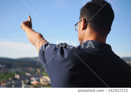 Man points towards the sky while looking out over a city landscape 142927233