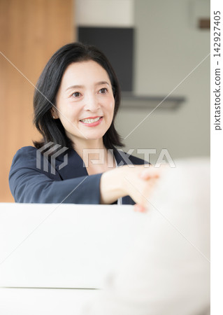 A Japanese middle-aged woman shakes hands with a smile; a female business professional in her 50s builds trust with her clients during business negotiations and contract signings. A Japanese middle-aged woman shakes hands with a smile; a female business professional in her 50s builds trust with her clients during business negotiations and contract signings. 142927405