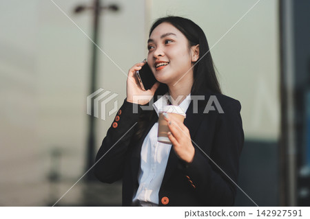 Business woman checks phone in front of modern building during the day Business woman checks phone in front of modern building during the day 142927591