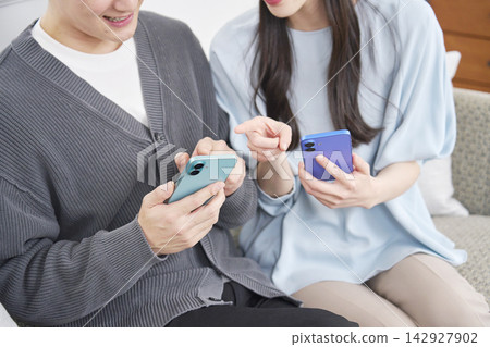 A couple using a smartphone in the living room (faceless) A couple using a smartphone in the living room (faceless) 142927902