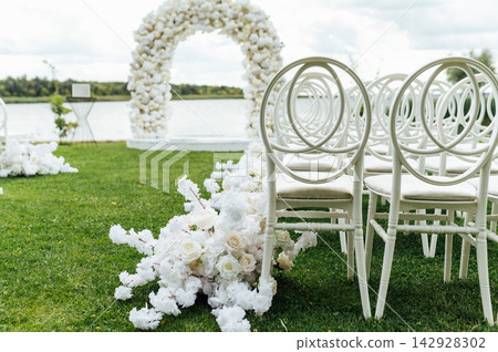 Wedding arch decorated with flowers and lights and white chairs for guests. Wedding ceremony. Wedding arch decorated with flowers and lights and white chairs for guests. Wedding ceremony. 142928302