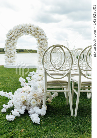 Wedding arch decorated with flowers and lights and white chairs for guests. Wedding ceremony. 142928303